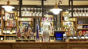 A bar area with multiple beer taps, a cash register, and shelves stocked with bottles and glasses. - The Bear Hotel by Greene King Inns (Hungerford)