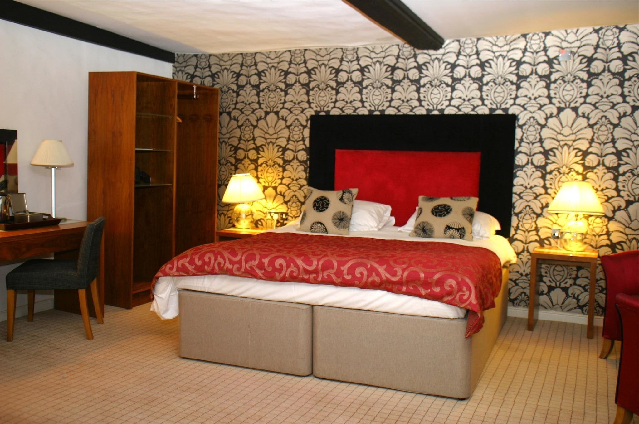 A bedroom with a bed, bedside lamps, a desk, and a wardrobe.