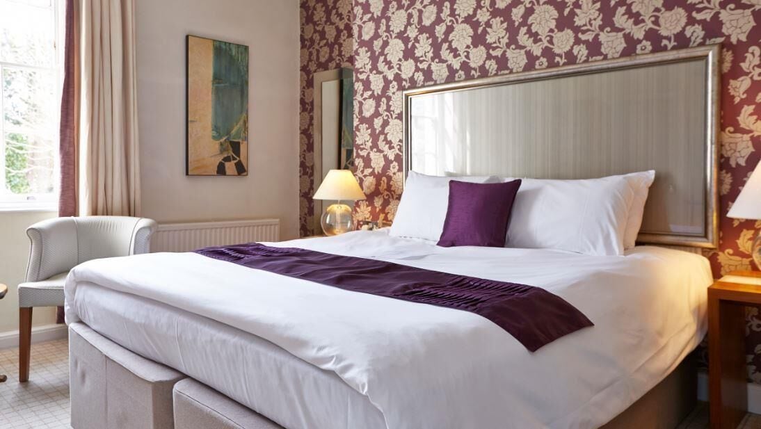 A hotel room with a large bed, a chair, a lamp, and a painting on the wall.