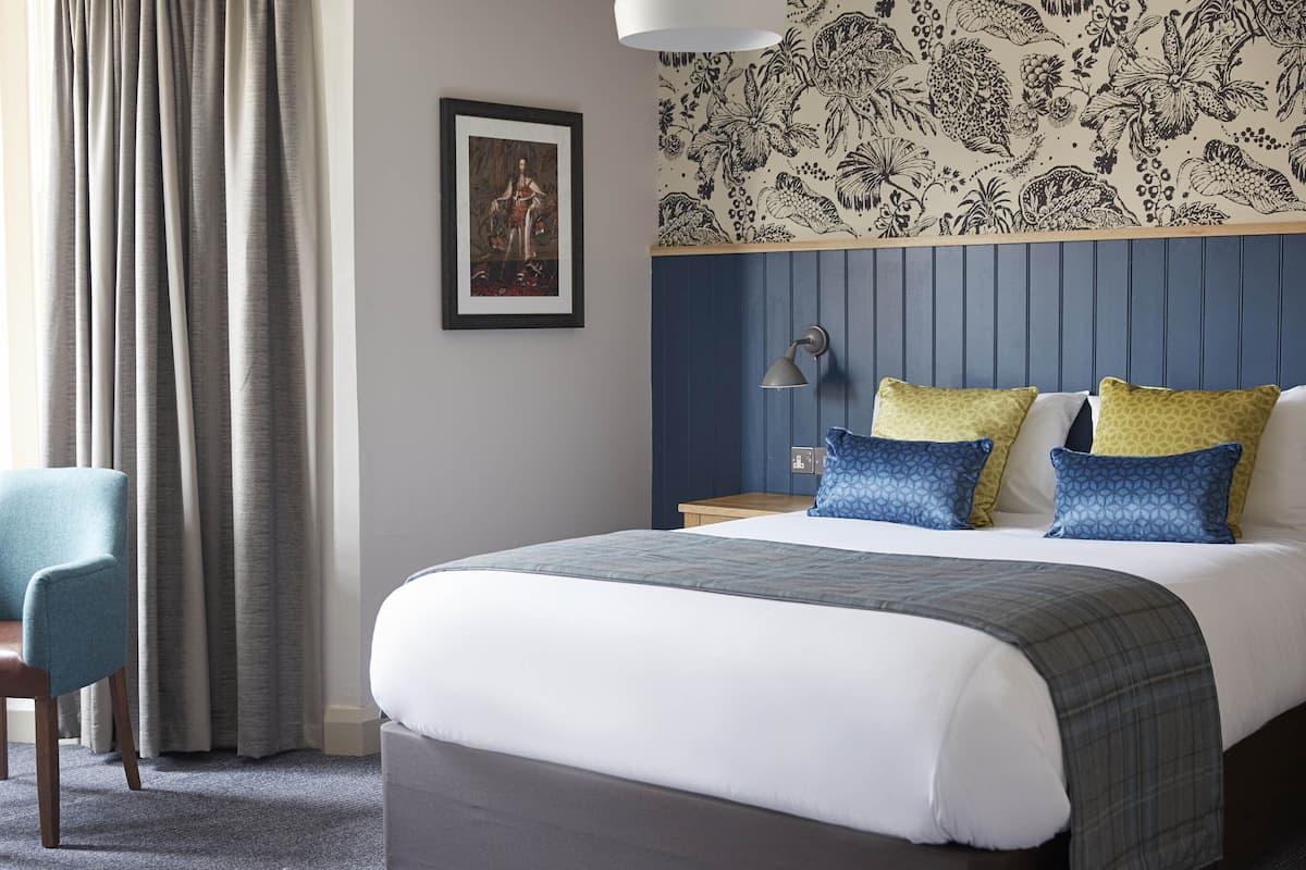 Una habitación de hotel con cama, escritorio, silla y mesita de noche con lámpara.