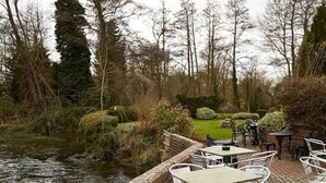 A riverside patio with outdoor seating and a wooden building in the background. - The Bear Hotel by Greene King Inns (Hungerford)