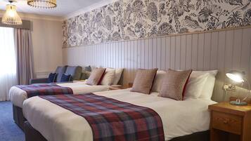 A hotel room with two beds, a desk, a chair, a lamp, and a patterned wallpaper.