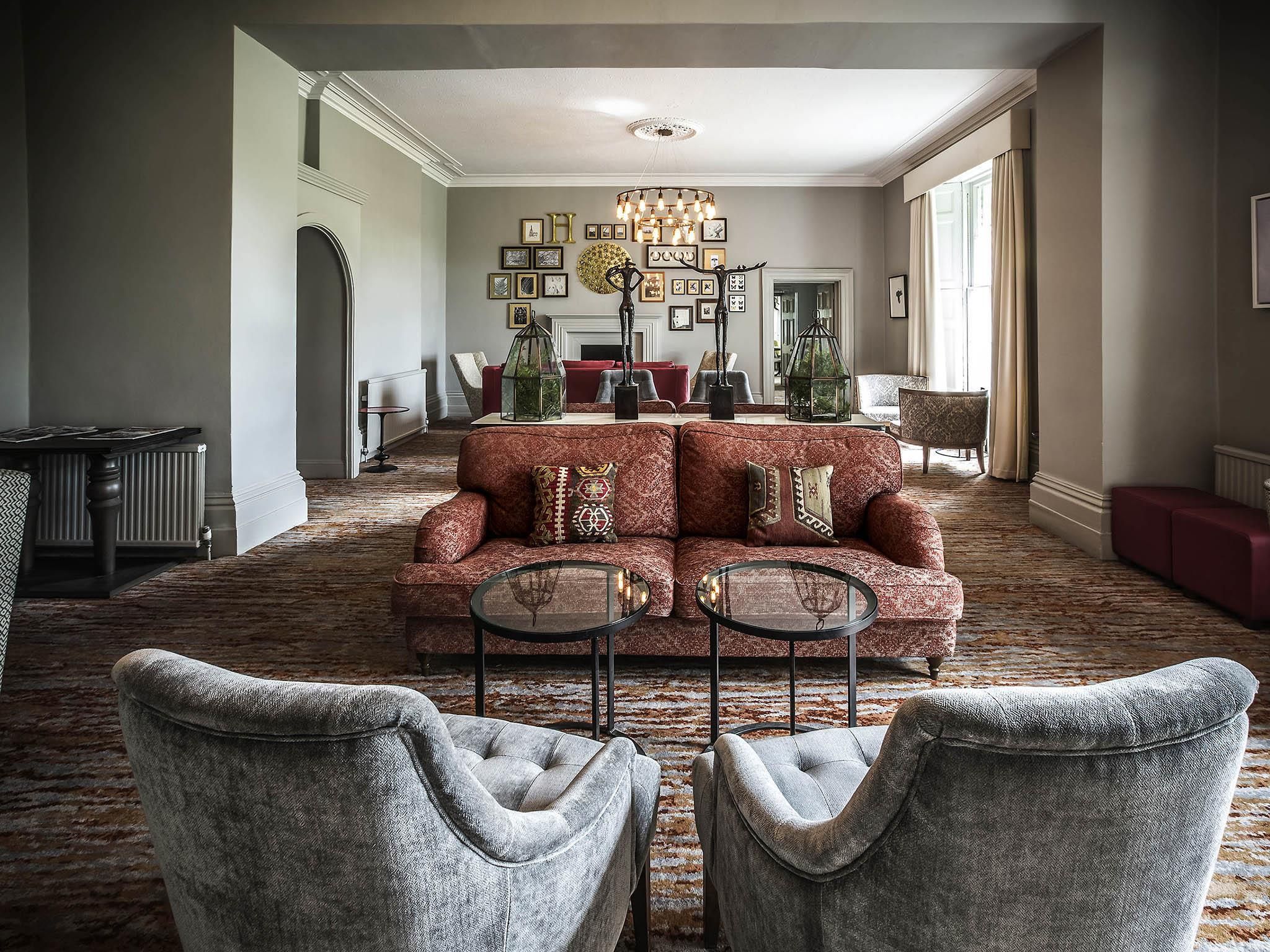 Un salón espacioso con un sofá rojo, dos sillones, una araña y una chimenea.
