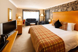 Habitación de hotel con una cama grande, televisor, escritorio con lámpara, sofá y una silla.