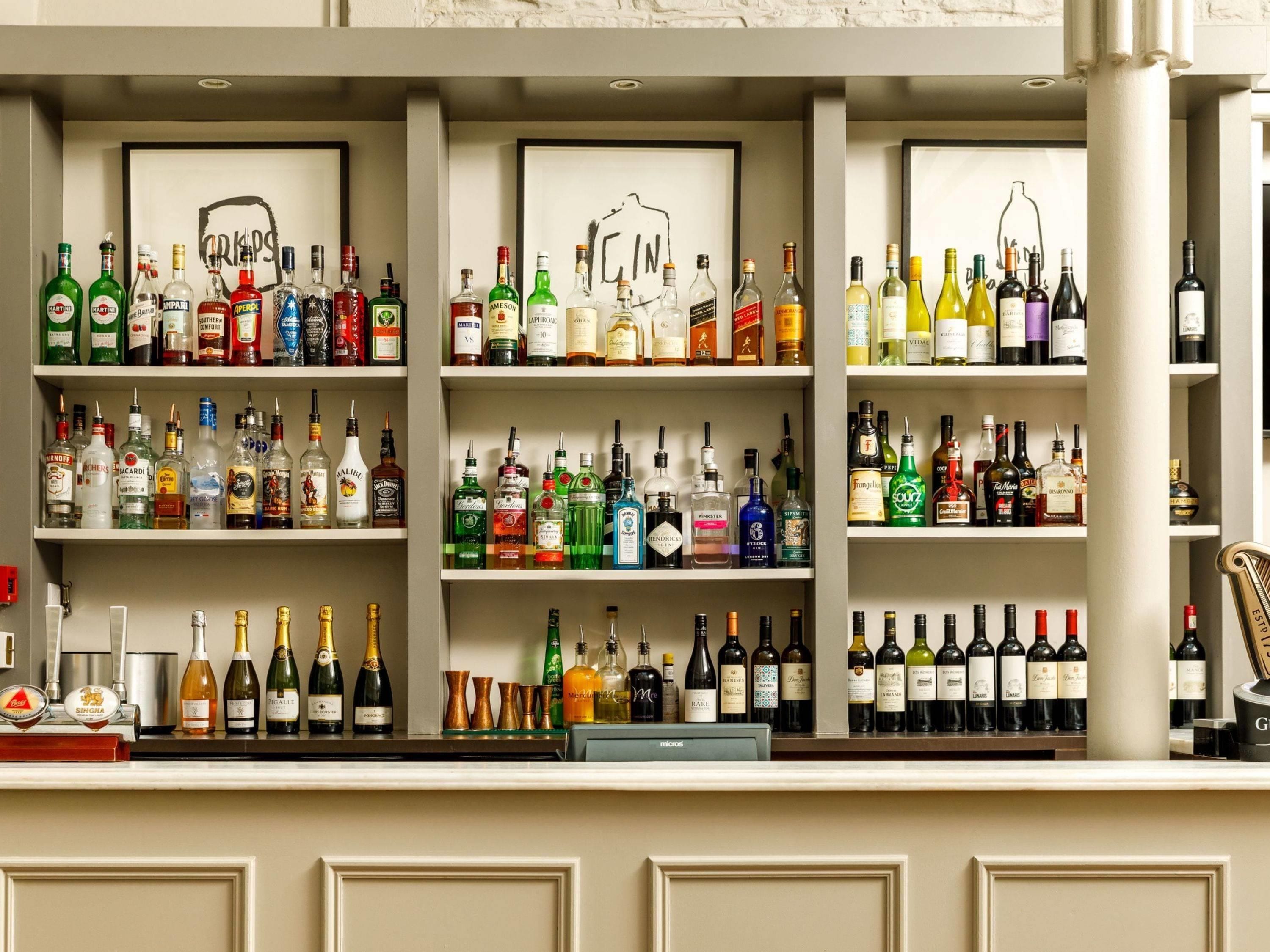Una zona de bar con estantes llenos de botellas de licores, una caja registradora y obras de arte enmarcadas en la pared.