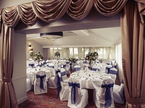 Une salle de banquet avec des tables rondes, des nappes blanches et des rubans bleus.