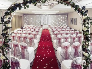 A hotel room with a red carpet aisle, white chairs with pink sashes, and a floral archway. - Mercure Bristol North The Grange Hotel (Bristol)