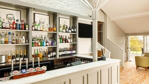 Zona de bar con estantes llenos de botellas de licores, una barra con grifos de cerveza y un televisor montado en la pared.