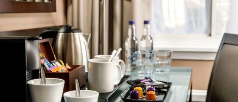 A hotel room with a kitchenette, including a coffee maker, cups, a tray with condiments, and a lamp.