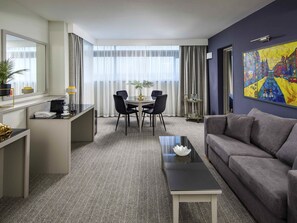 A hotel room with a dining area, a sofa, a coffee table, and a painting on the wall. - Mercure Manchester Piccadilly Hotel (Manchester)