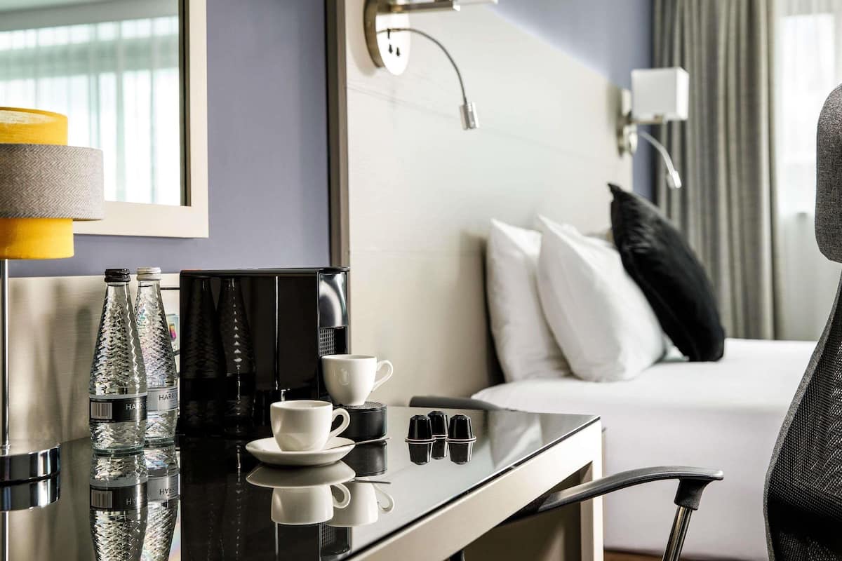 Une chambre d’hôtel avec un lit, une table de chevet sur laquelle se trouvent une tasse, une bouteille et une télécommande.