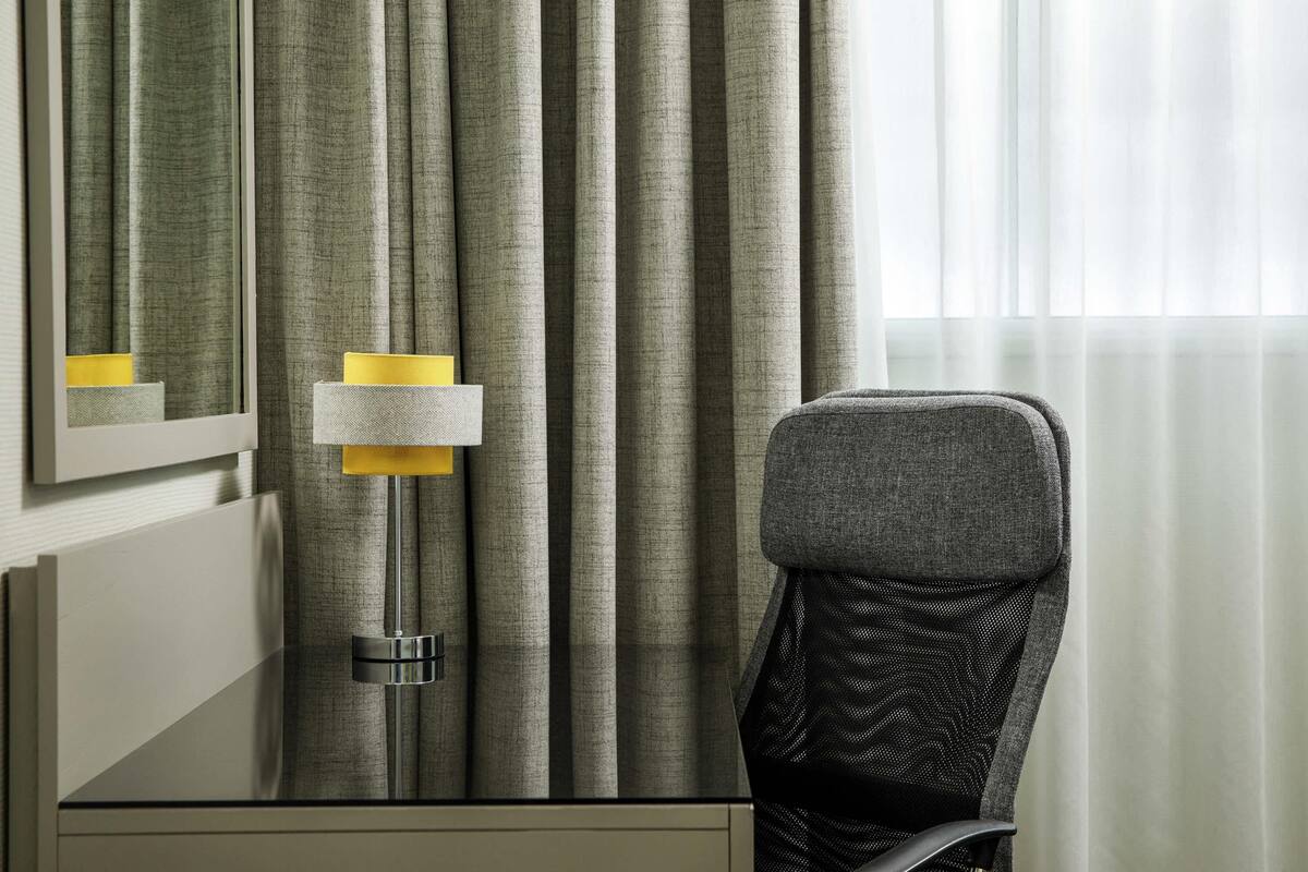 Ein Hotelzimmer mit Bett, Nachttisch, Lampe und Vorhängen.