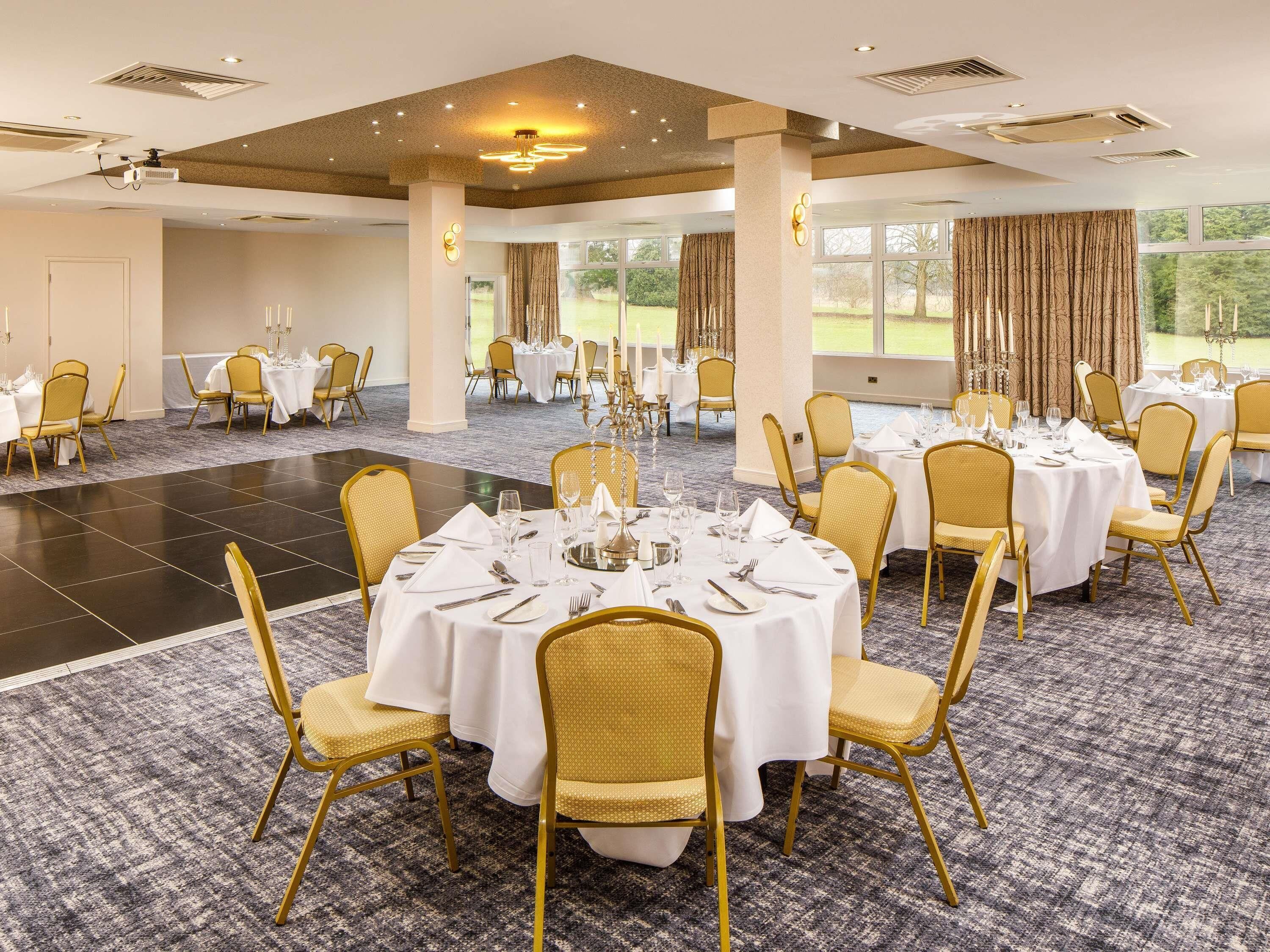 A banquet hall with round tables, gold chairs, and white tablecloths.