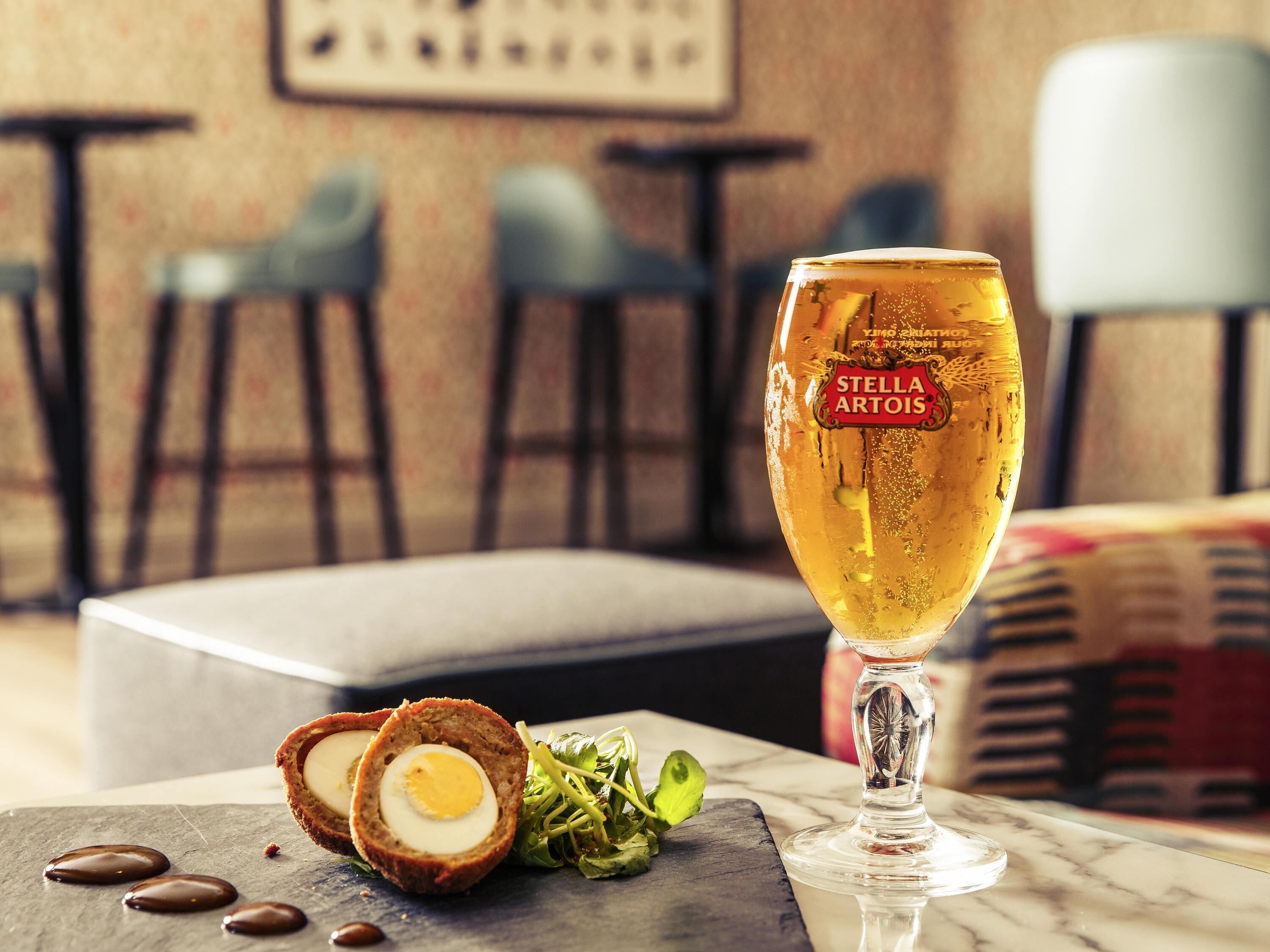 A glass of beer with a label, a scotch egg, and a green salad on a marble surface.