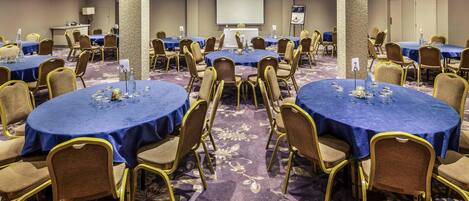 Un salón de conferencias con mesas redondas, sillas y una pantalla para proyector.
