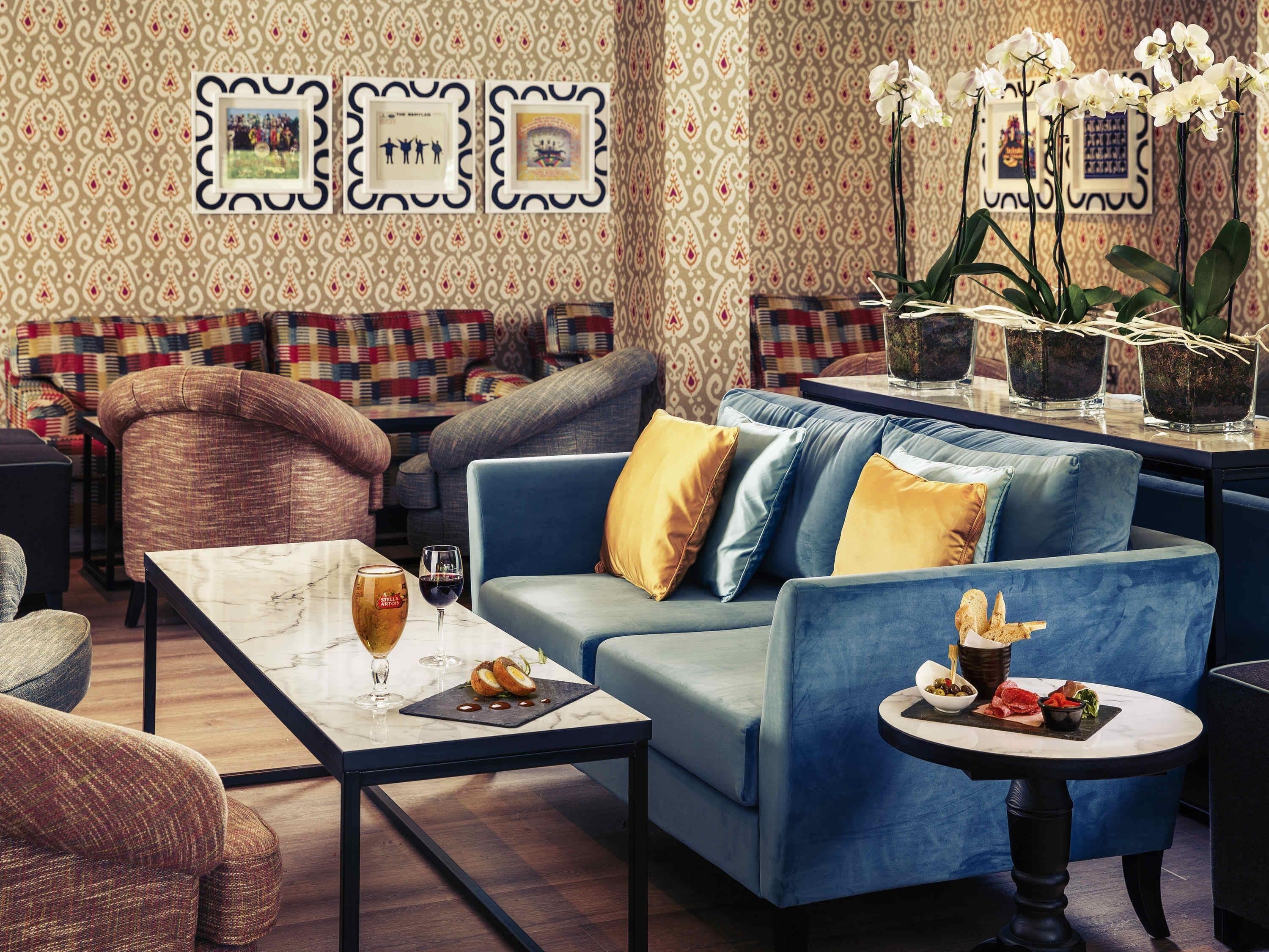 Un área de estar moderna con un sofá, sillones, una mesa de centro y elementos decorativos como cuadros enmarcados y plantas en macetas.