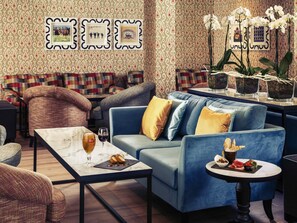 A modern living room with a blue sofa, patterned wallpaper, and a coffee table with a wine glass and snacks. - Mercure Maidstone Great Danes Hotel (Maidstone)