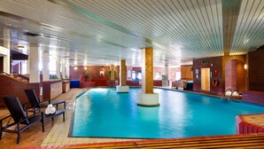 Una piscina interior con sillones de descanso y una zona de terraza de madera.