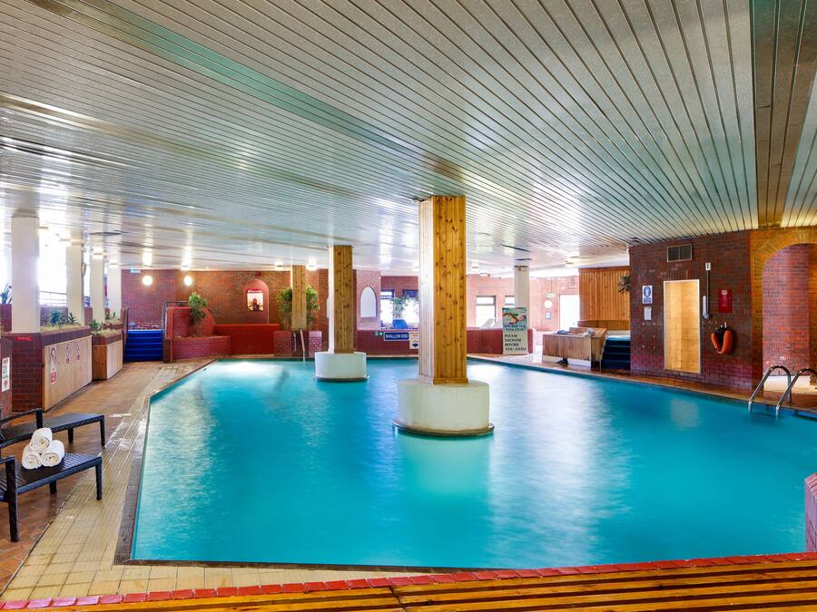 An indoor swimming pool with lounge chairs and a wooden deck area.