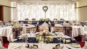 Un salón de banquetes con mesas redondas, manteles blancos y cintas azules.