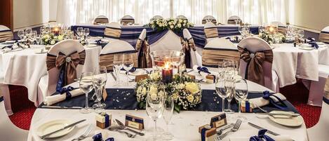 A banquet hall with round tables, white tablecloths, and blue sashes.