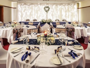 Un salón de banquetes con mesas redondas, manteles blancos y cintas azules.