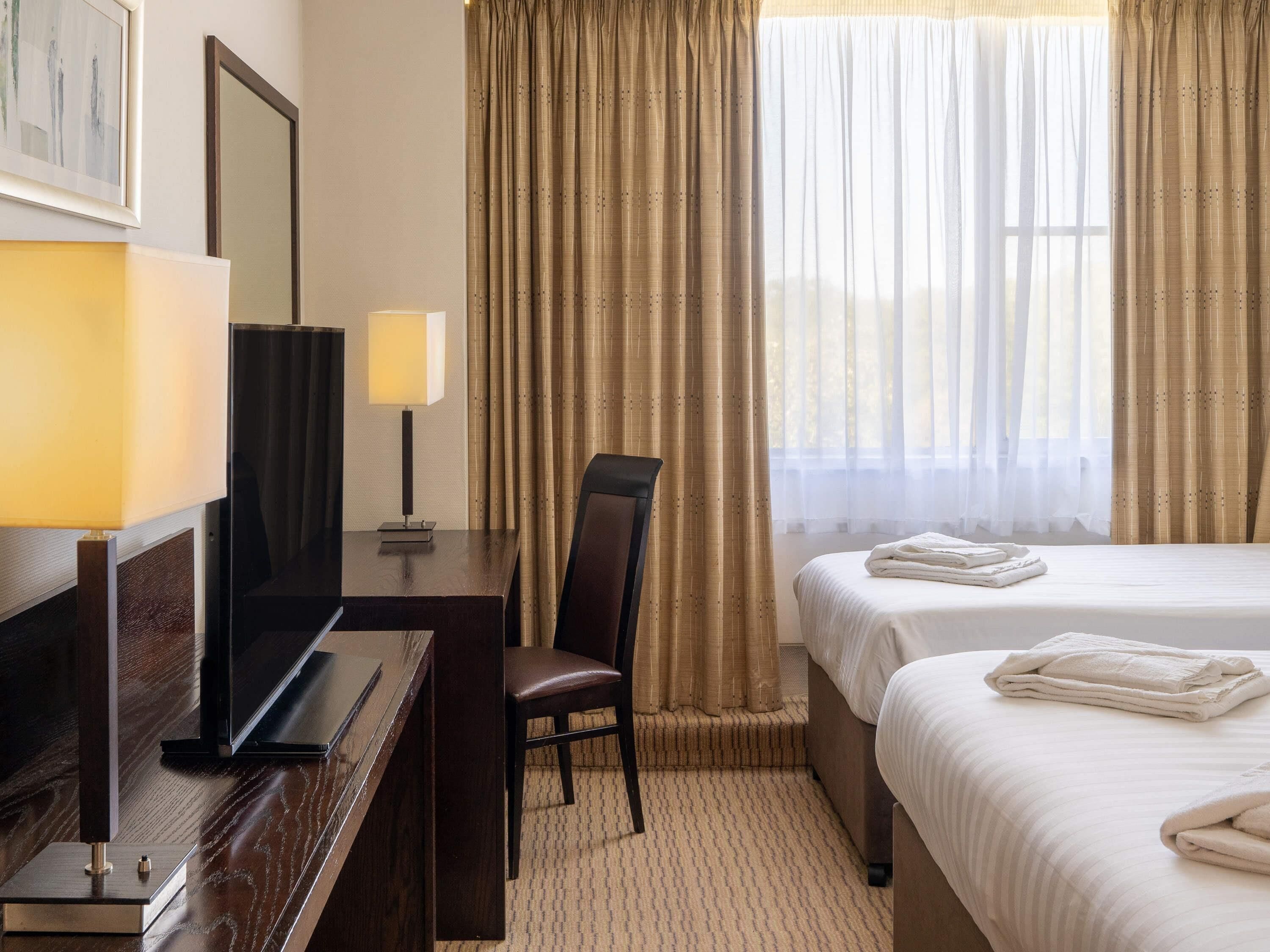 Habitación de hotel con una cama, un escritorio con lámpara, una silla y un televisor.