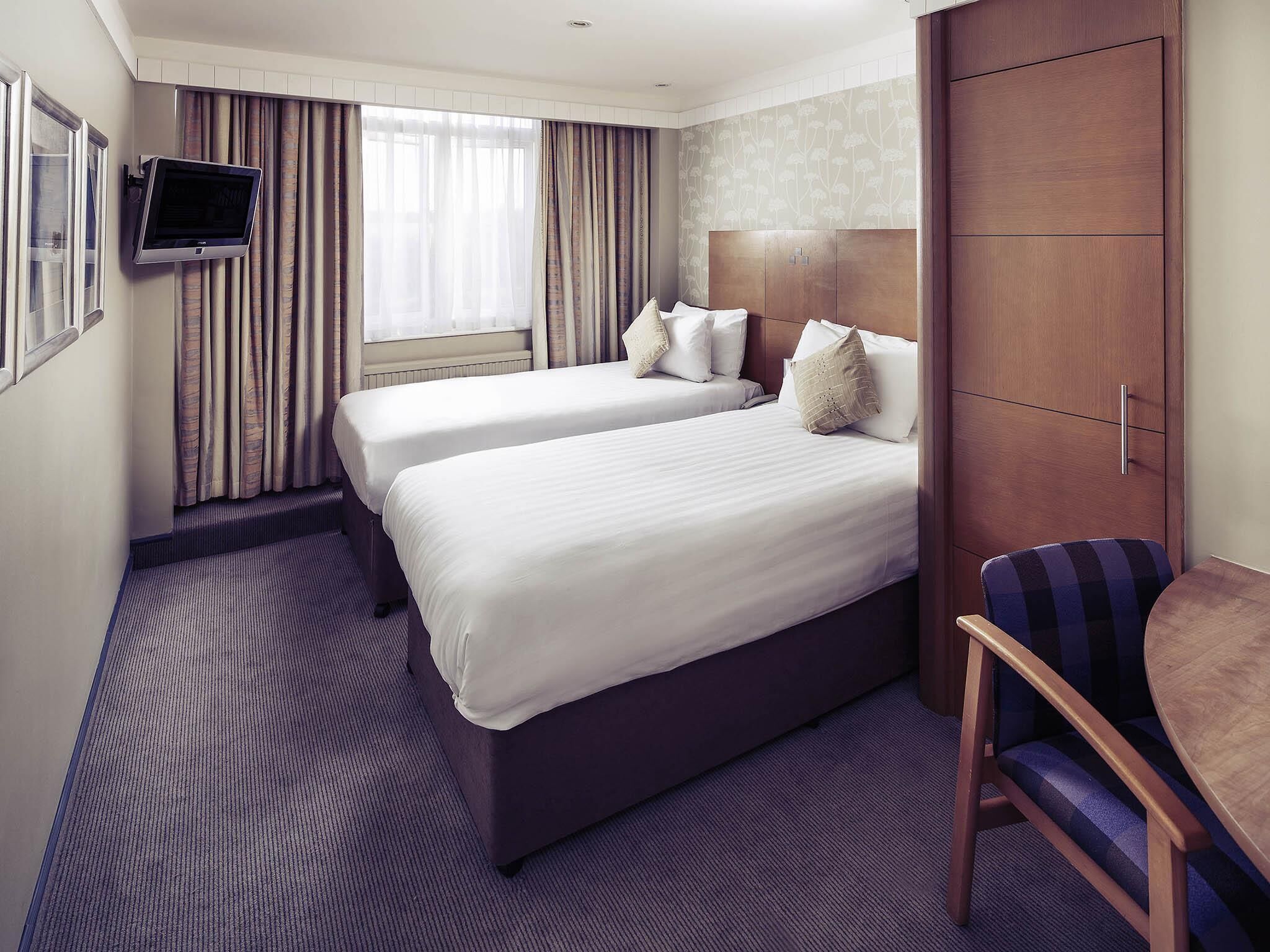 A hotel room with two beds, a television, a wardrobe, and a chair.