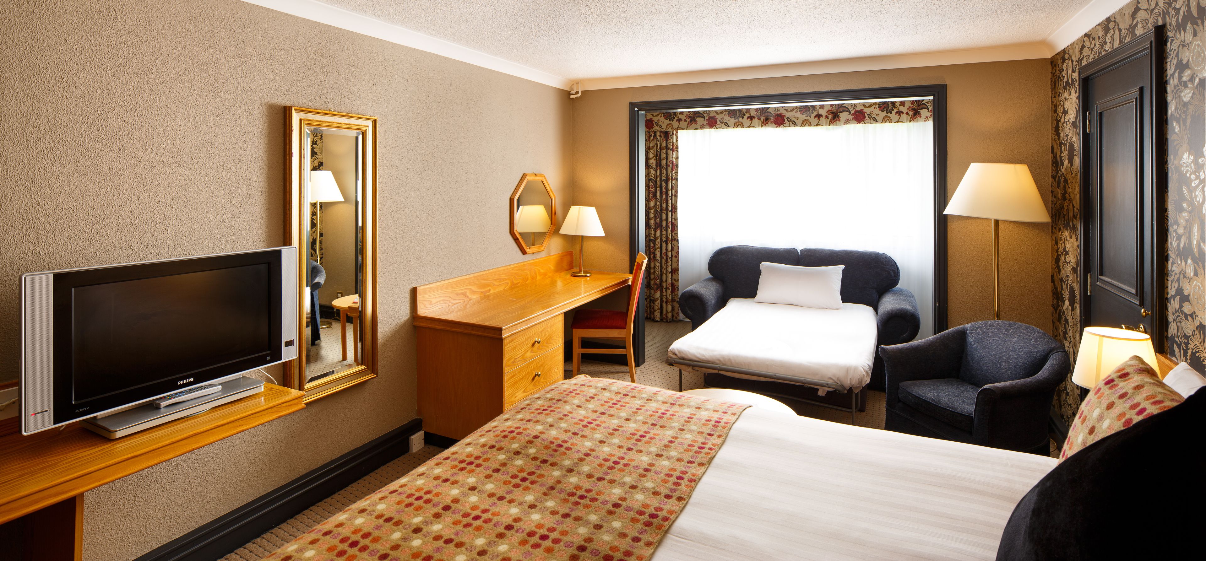 A hotel room with a bed, a desk, a television, a chair, and a window with curtains.