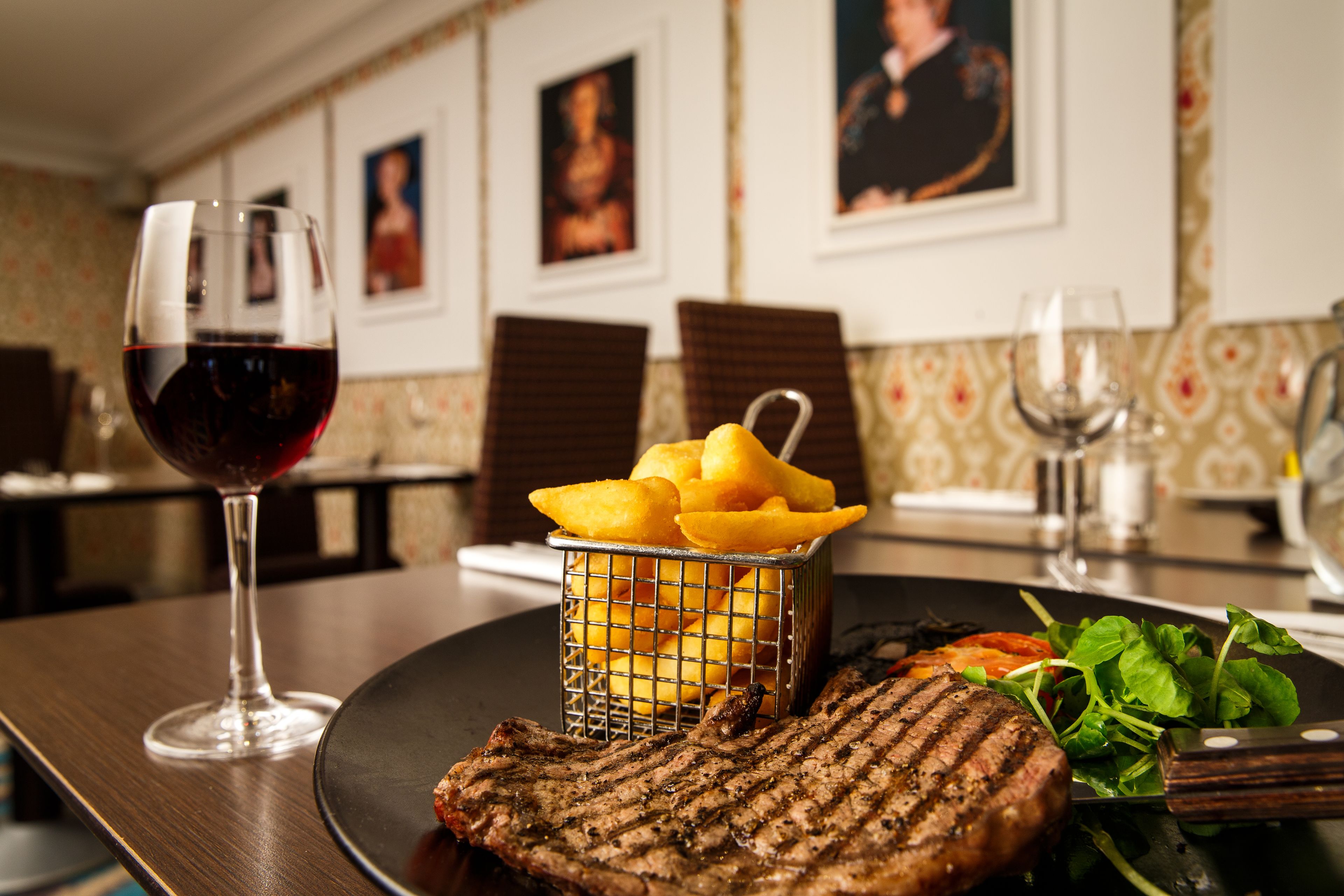 Una mesa de comedor con un bistec a la parrilla, una copa de vino tinto, una cesta de papas fritas y una ensalada.