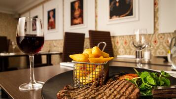 Una mesa de comedor con un bistec a la parrilla, una copa de vino tinto, una cesta de papas fritas y una ensalada.