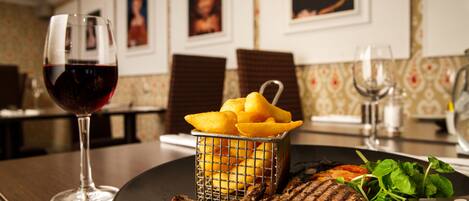 Una mesa de comedor con un bistec a la parrilla, una copa de vino tinto, una cesta de papas fritas y una ensalada.