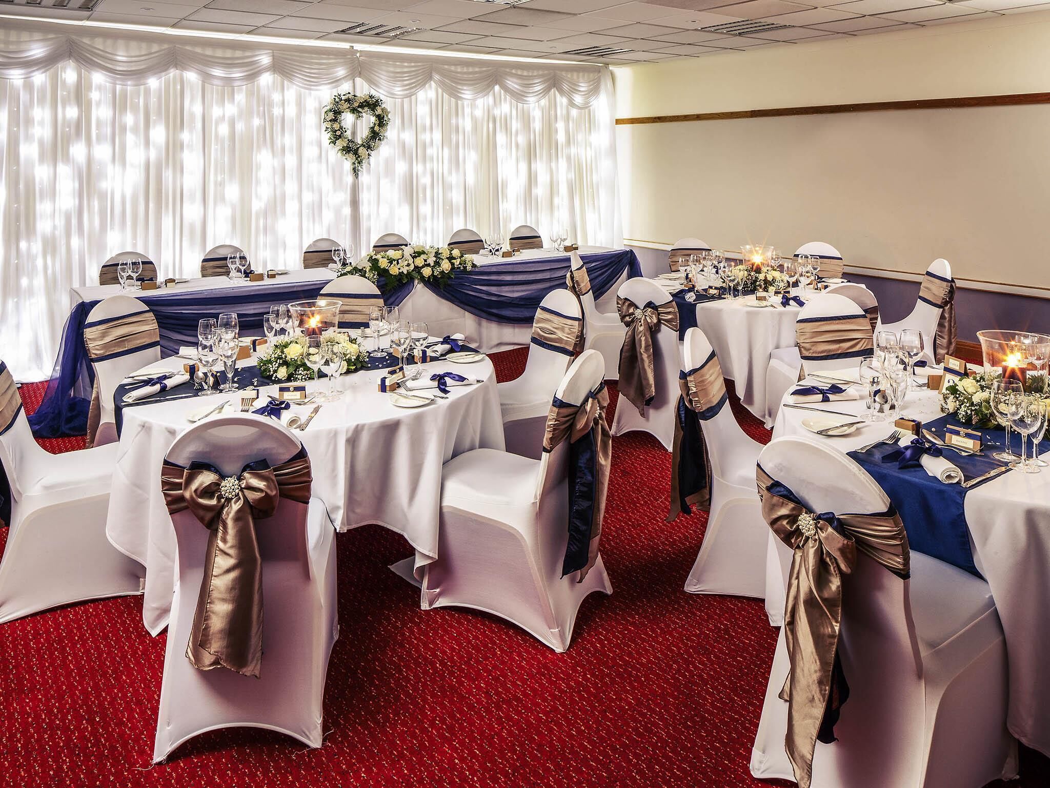 A banquet hall with round tables, white tablecloths, and chairs with gold sashes.