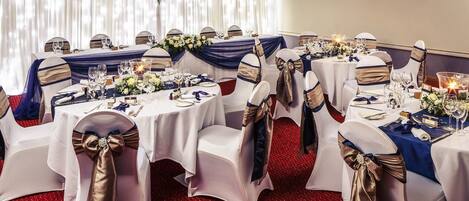 A banquet hall with round tables, white tablecloths, and chairs with gold sashes.