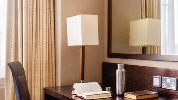 Escritorio de habitación de hotel con una lámpara, un libro, una botella y un espejo.