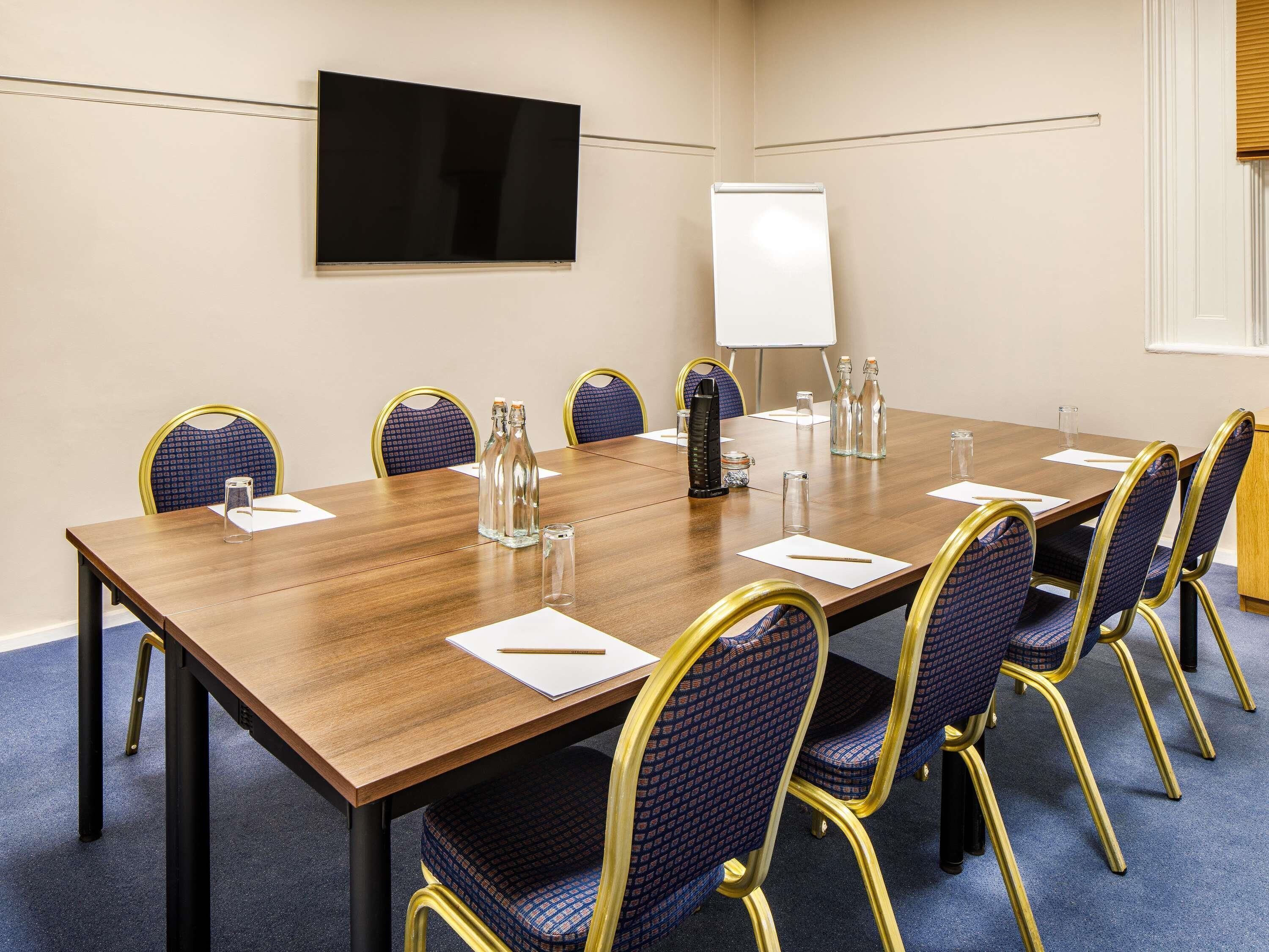 Une salle de conférence avec une longue table, des chaises, un tableau blanc et un téléviseur fixé au mur.