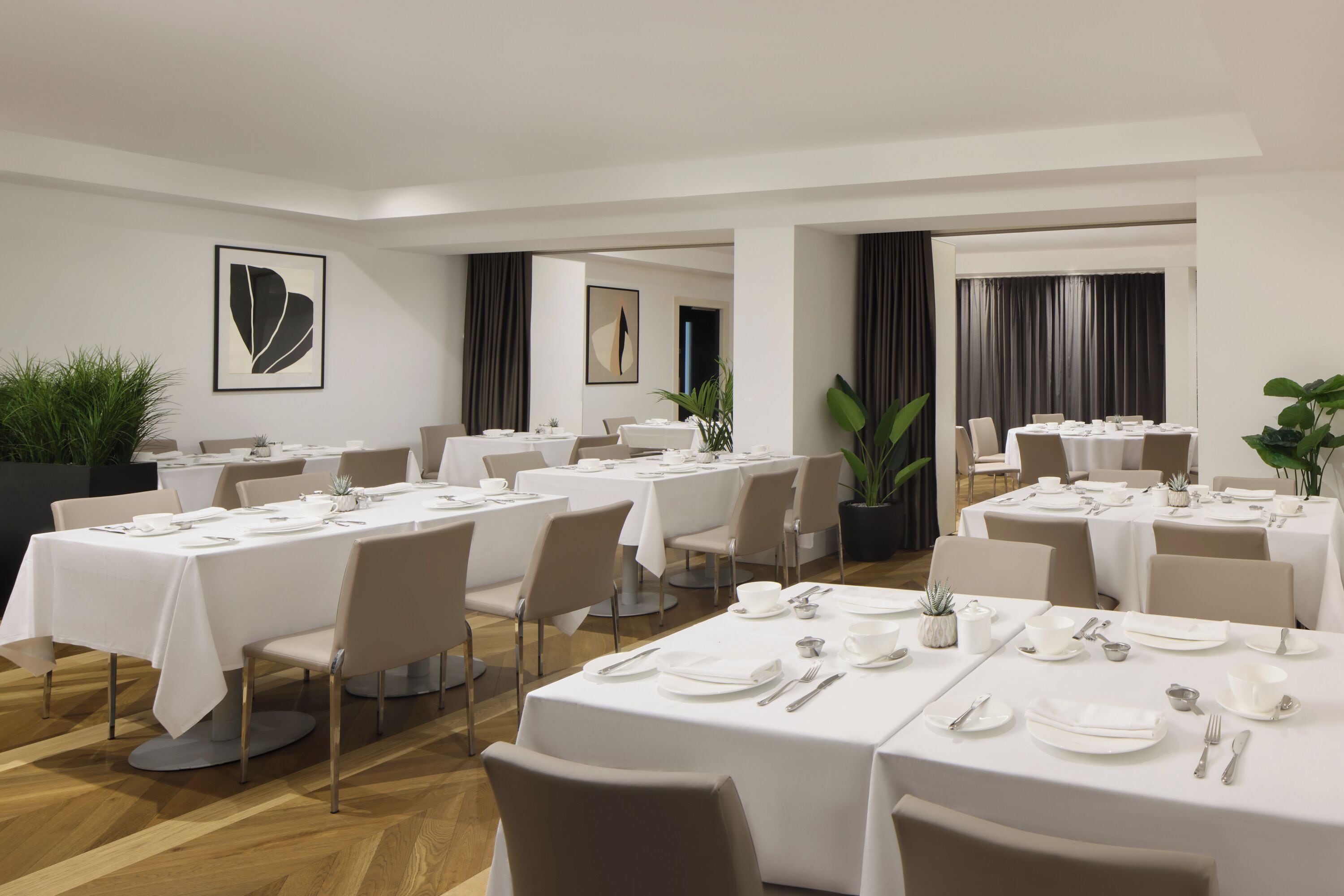 Un espace repas avec plusieurs tables dressées, présentant un design épuré et moderne, avec des nappes blanches et des chaises aux couleurs neutres.