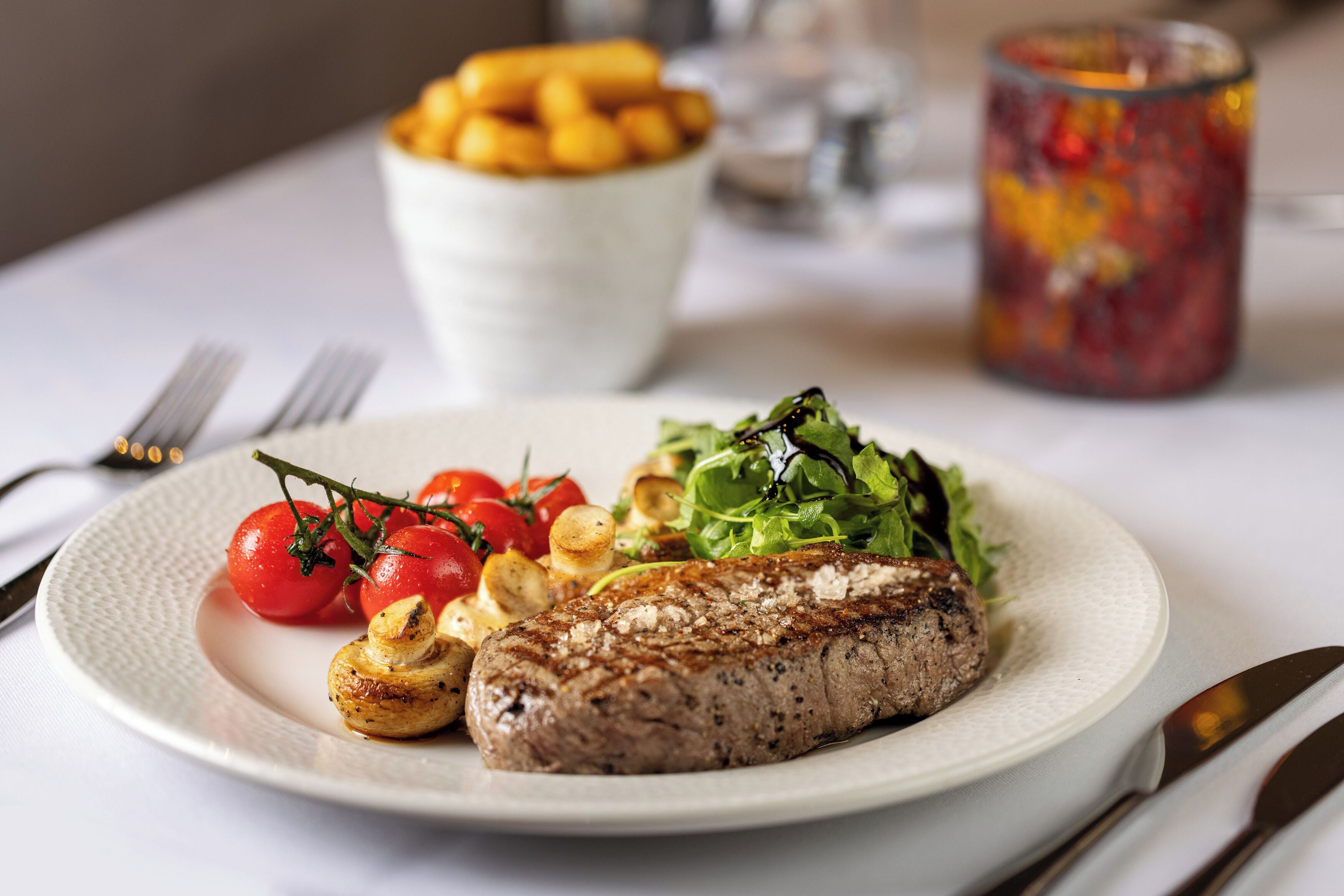 A plate with grilled steak, roasted potatoes, cherry tomatoes, and a side salad.