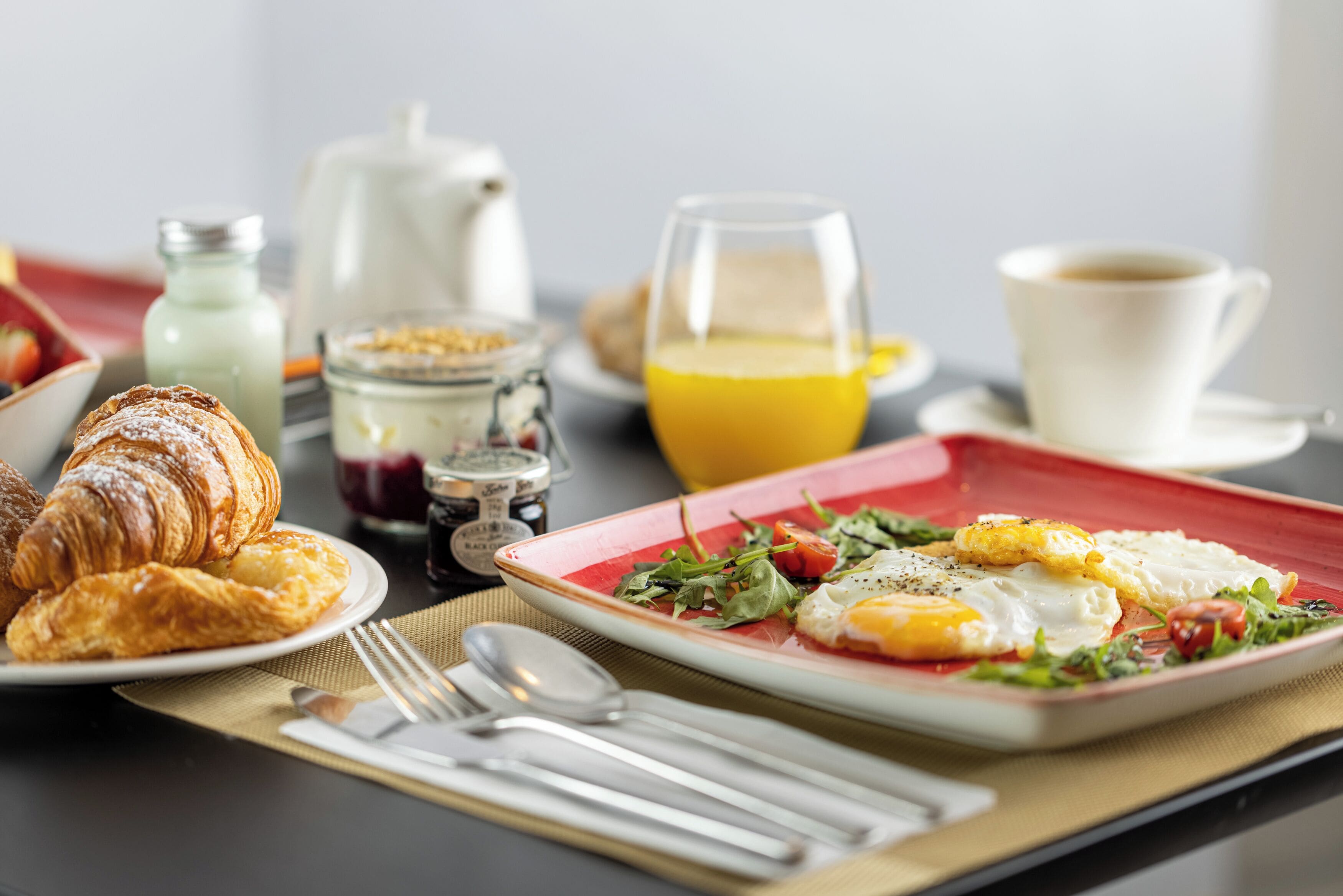 A breakfast setting with croissants, eggs, and a glass of orange juice on a table.