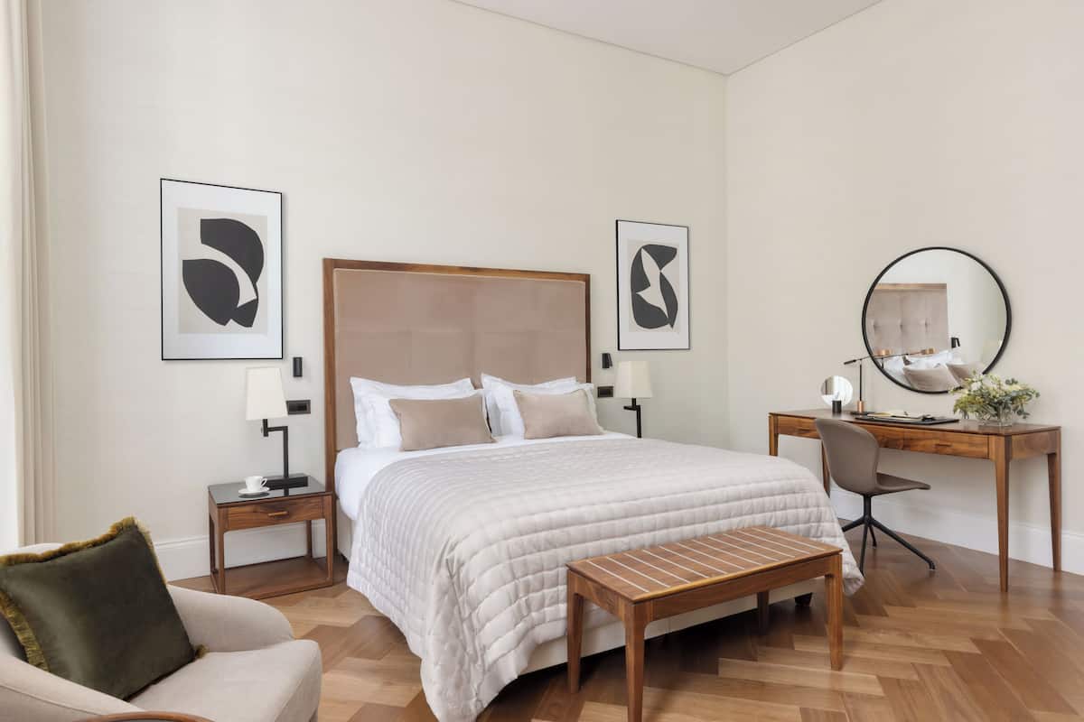 Una habitación de hotel moderna con una cama grande, un escritorio de madera, una silla y dos mesitas de noche con lámparas.