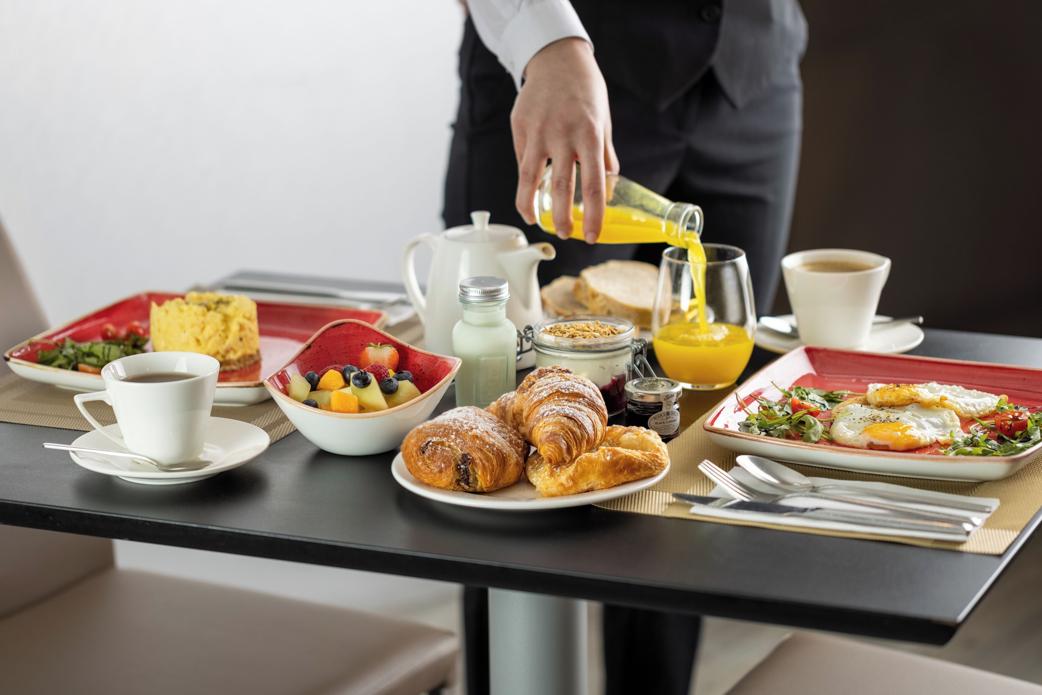 A breakfast table with croissants, fruit, coffee, and juice.