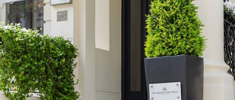 A black planter with a label reading "The Queen's Gate Hotel London" and a neatly trimmed topiary.