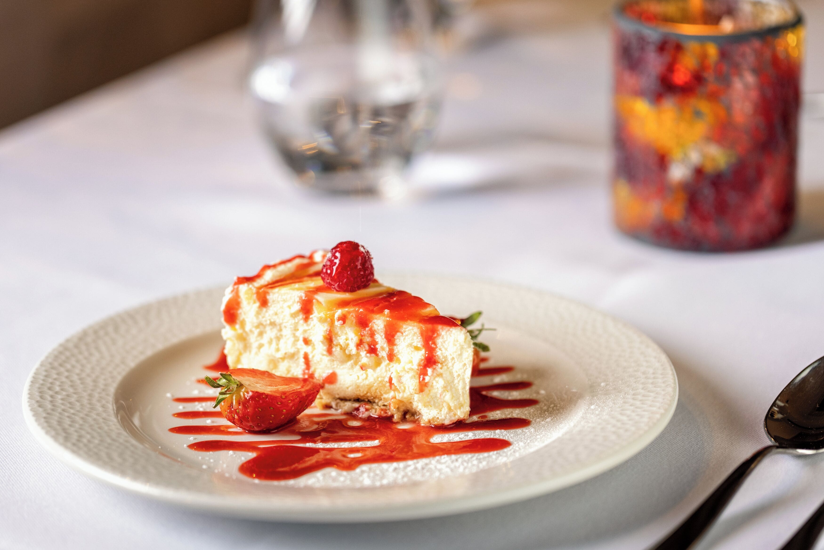A dessert on a plate with a strawberry and a spoon nearby.