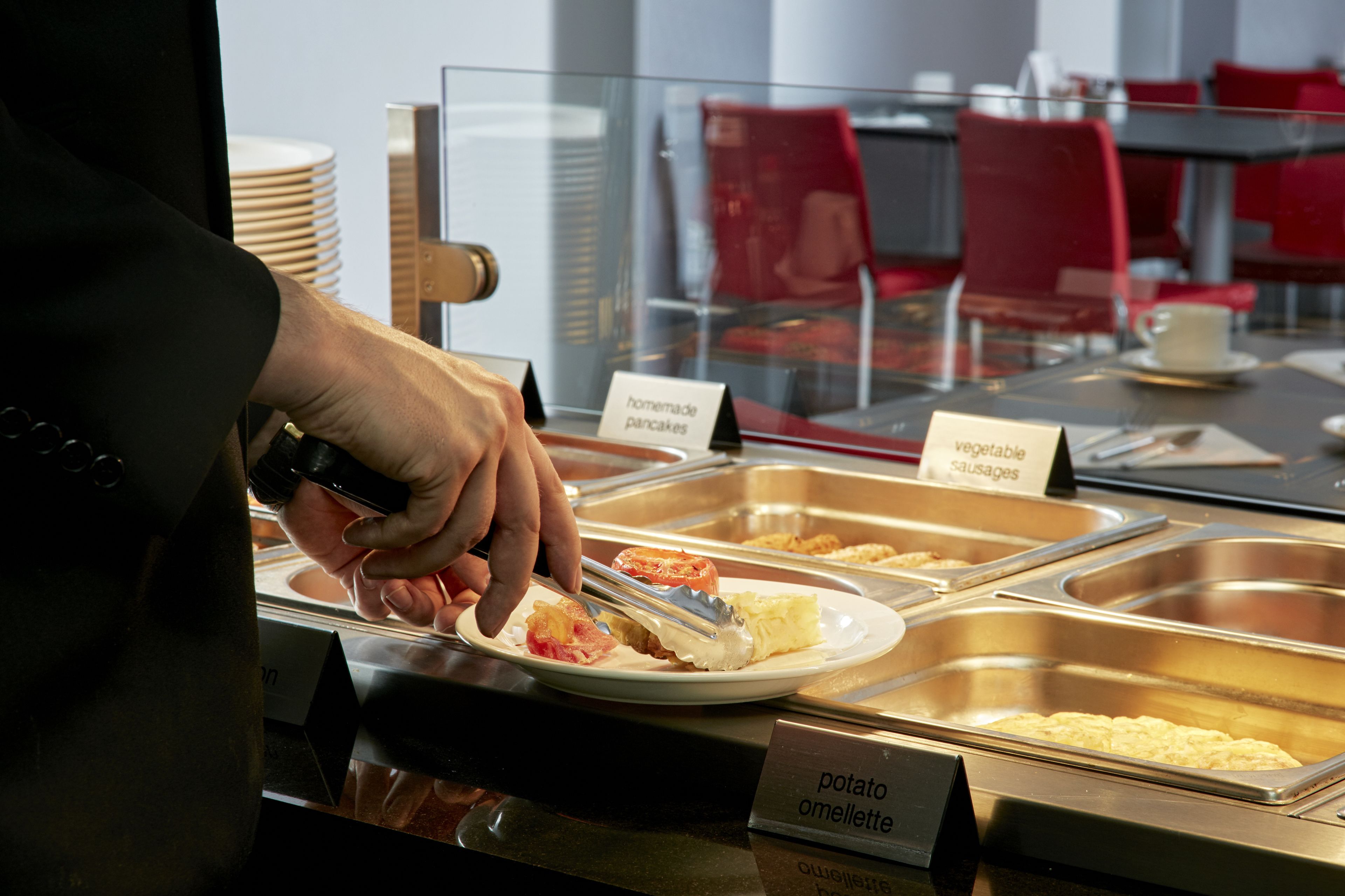 Un espace buffet avec différentes sections de nourriture clairement identifiées, comprenant des « crêpes faites maison », des « saucisses végétales » et une « omelette aux pommes de terre ».