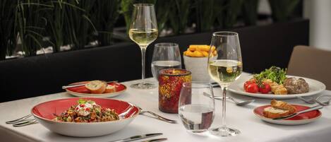 A dining table set with various dishes, glasses, and cutlery, surrounded by indoor plants.