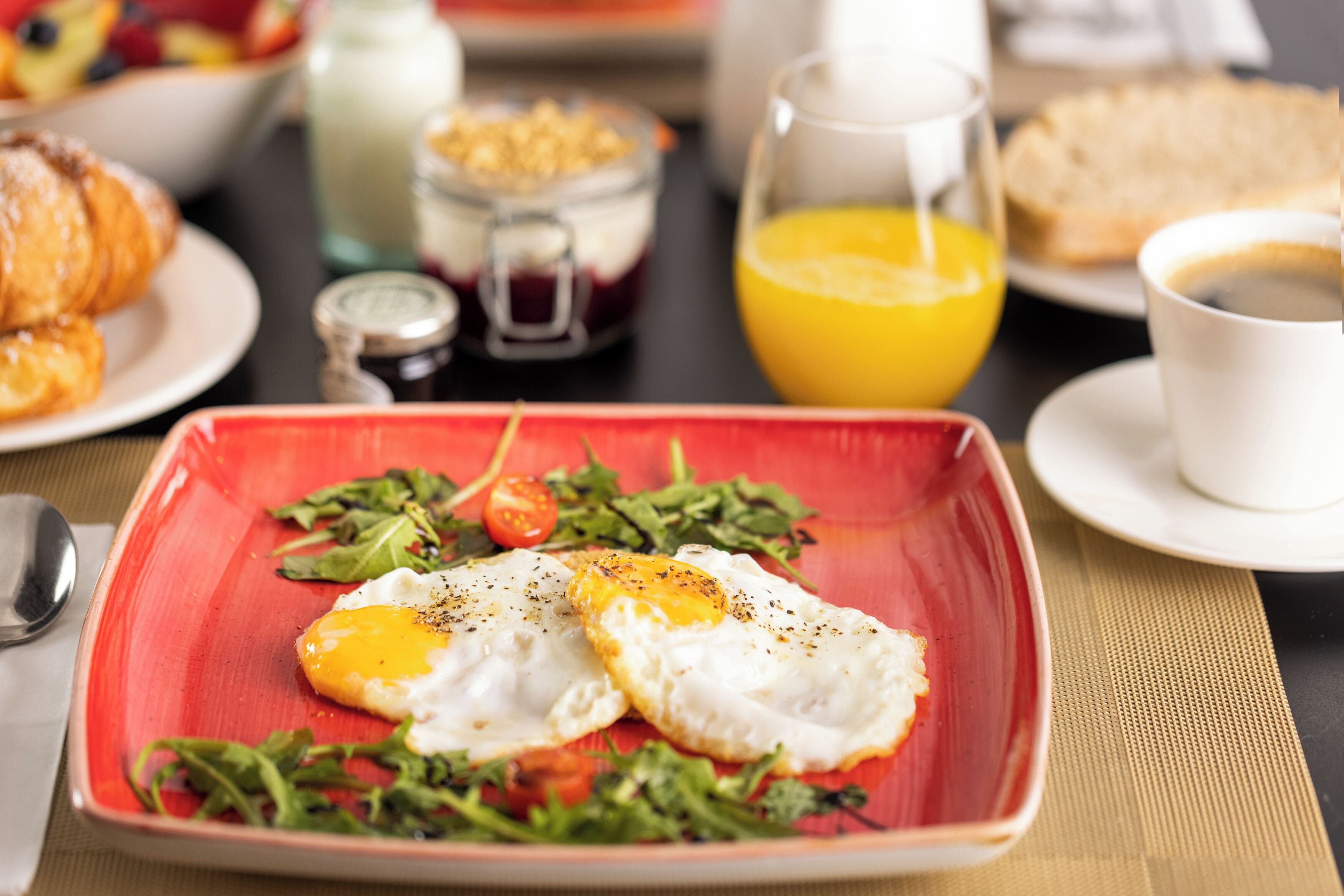 A breakfast setting with a plate of eggs, greens, and tomatoes, a glass of orange juice, and a cup of coffee.