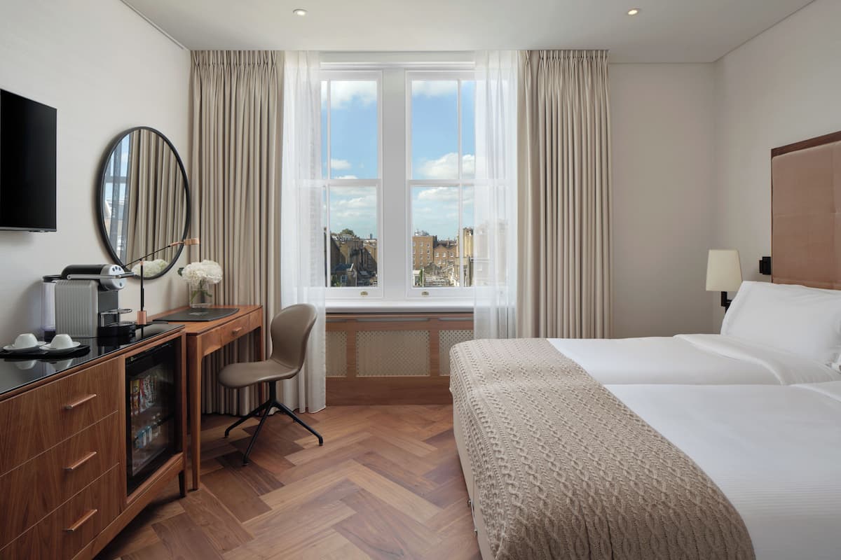 Habitación de hotel con cama, escritorio con computadora, silla, televisor y ventana con cortinas.