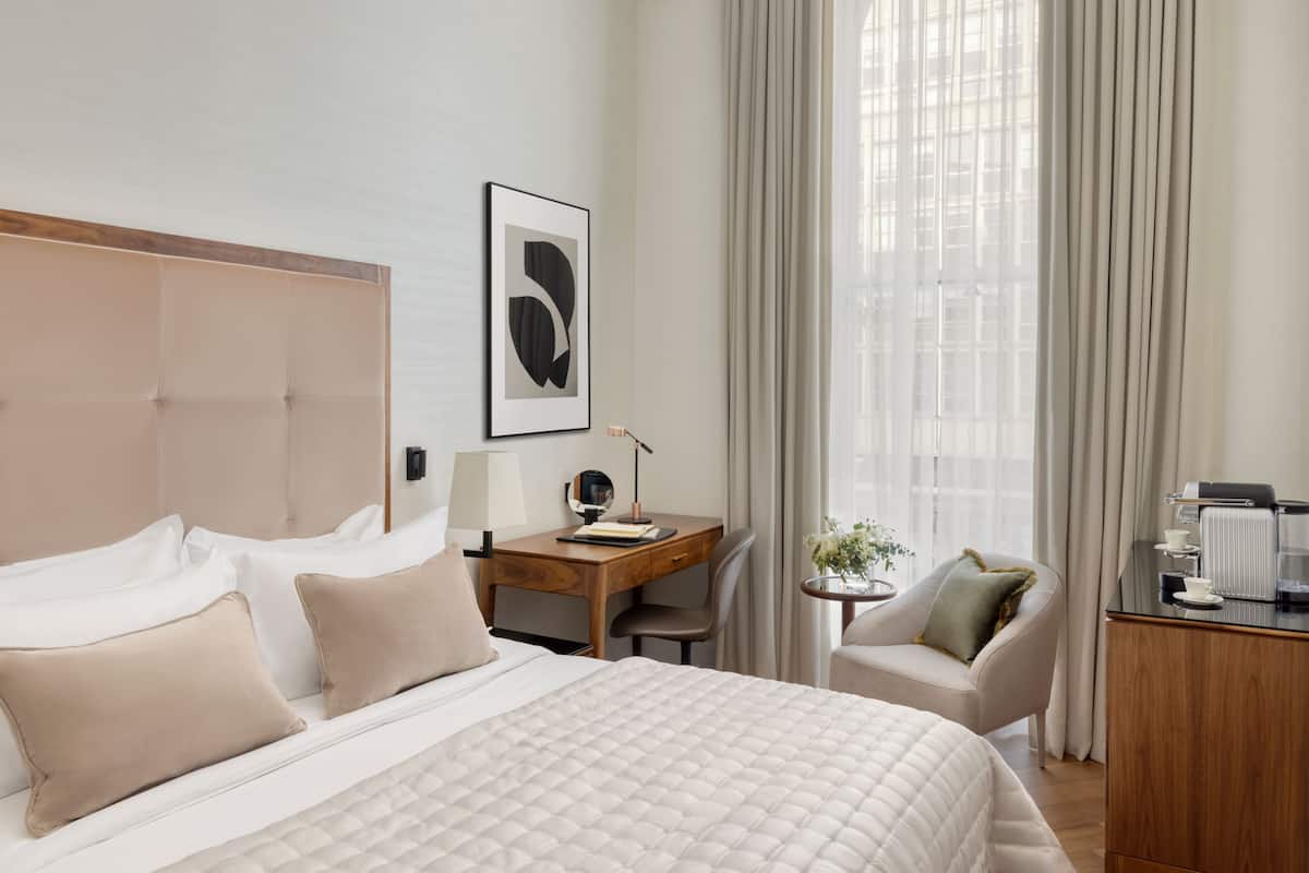 Habitación de hotel con cama, escritorio, silla y una mesita con una planta.