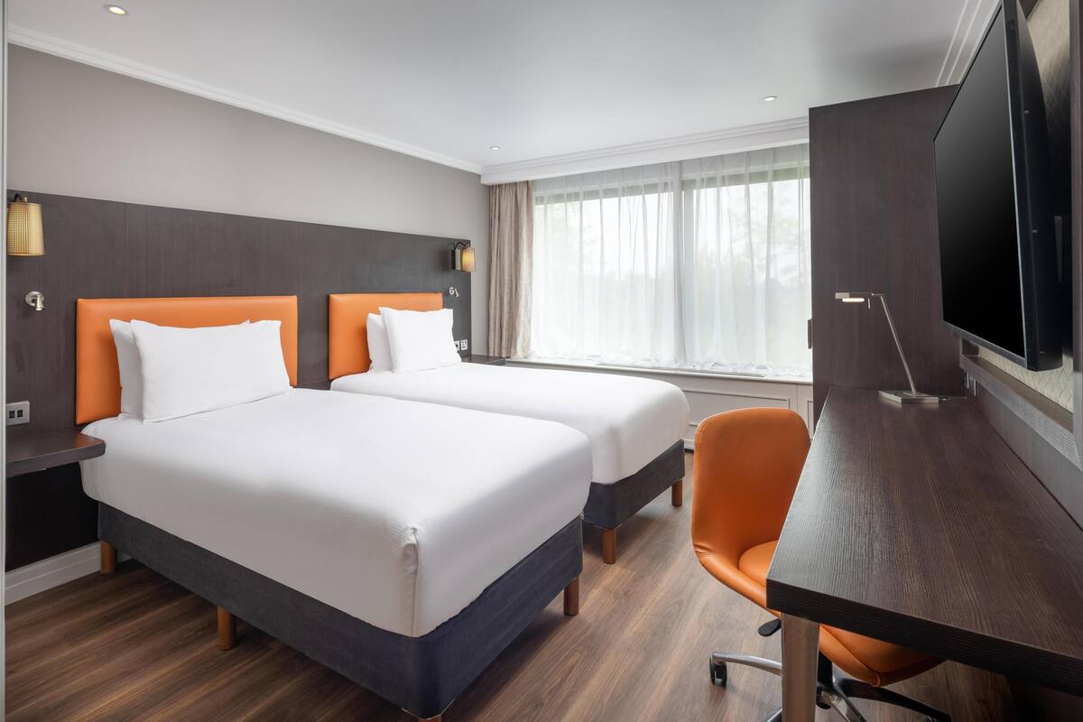 Una habitación de hotel con dos camas, un escritorio, un televisor y una ventana con cortinas.