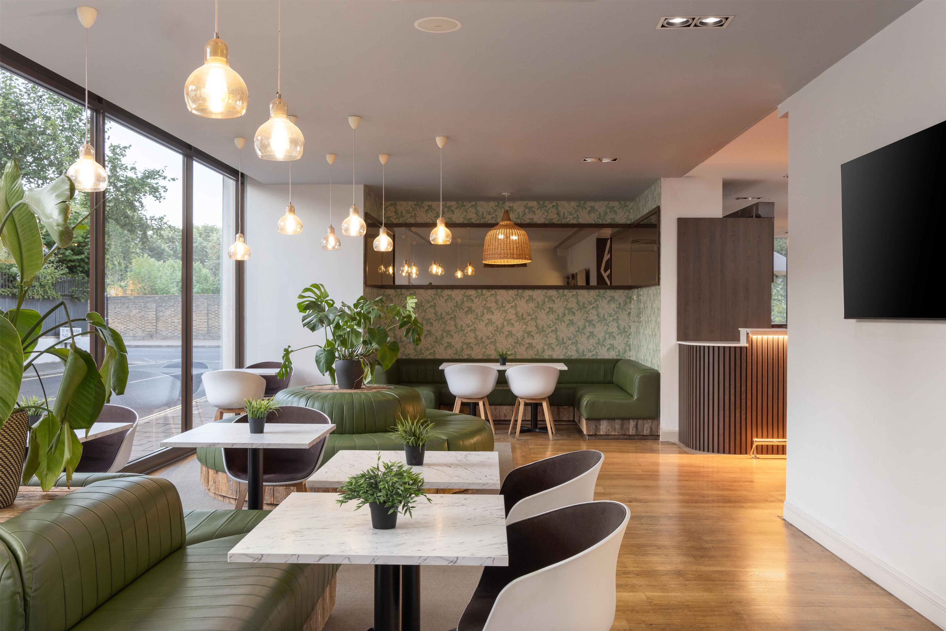 Ein modernes Interieur mit grünen Sitzgelegenheiten, weißen Tischen und hängenden Pendelleuchten.